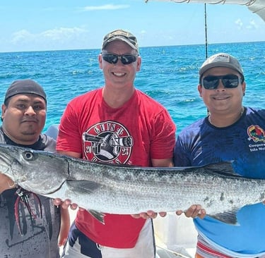 Smiling fishermen holding a large barracuda on a deep sea fishing charter boat in tropical blue waters.