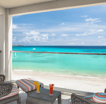 Luxury resort balcony overlooking a tropical turquoise beach with cocktails on a table.