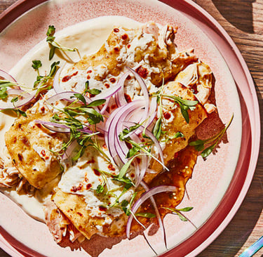 Shredded chicken enchiladas suizas topped with white cream sauce, red onions, and fresh cilantro.