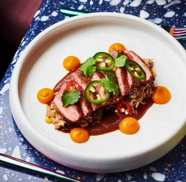 Seared duck breast sliced with mole sauce, jalapeños, and squash purée on a terrazzo table.