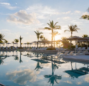 Luxury tropical resort pool with lounge chairs and palm trees reflecting in the water at sunset.