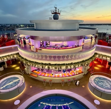 Luxury cruise ship pool deck with illuminated circular bars and hot tubs at sunset.