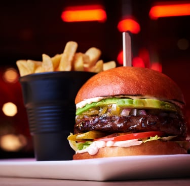 Gourmet beef burger with avocado, pickles, and red onion served with a side of crispy golden fries.