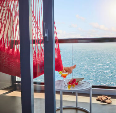 Relaxing on a luxury cruise ship balcony in a red hammock with ocean views and a tropical cocktail.