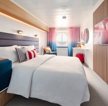 Modern cruise ship cabin with a king-size bed, porthole window, and contemporary decor.