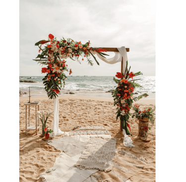 Tropical beach wedding altar with colorful floral arrangements and white draping on a sandy shore.