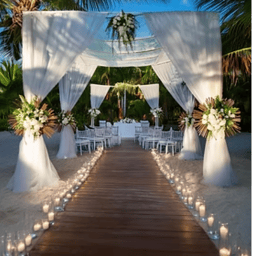 Elegant beach wedding ceremony setup with a white draped altar, floral arrangements, and a candlelit wooden walkway.