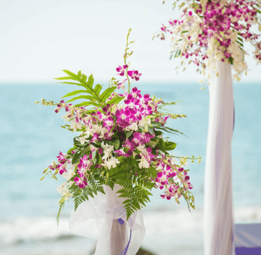 Purple and white orchid floral arrangements for a beach wedding ceremony with ocean background.