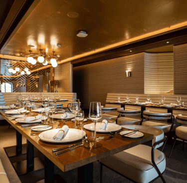 Elegant luxury cruise ship dining room with modern wooden tables and white leather chairs.
