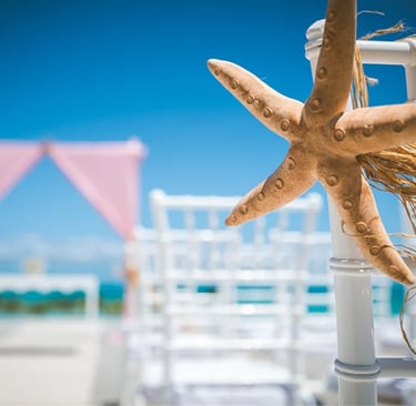 A starfish chair decoration at a tropical beach wedding ceremony with pink altar and white chairs.