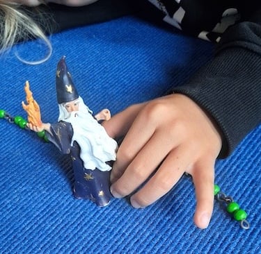 Kinderhand mit Zauberer, der anhand einer Perlenkette die Schritte des 1x1 abgeht.