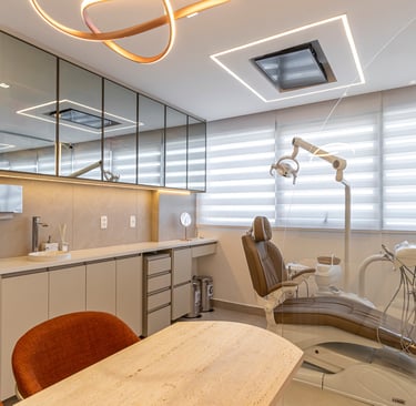 Consultório sofisticado com bancada de pedra clara, armários espelhados e cadeira odontológica.