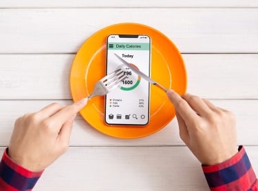 Person using a calorie counter app on a smartphone on a plate to track daily nutrition and diet.