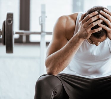 Frustrated muscular man sitting in a gym holding his head after an exhausting workout session.