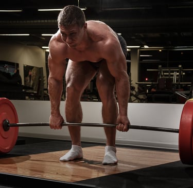 Muscular bodybuilder performing a heavy barbell deadlift exercise on a platform in a gym.
