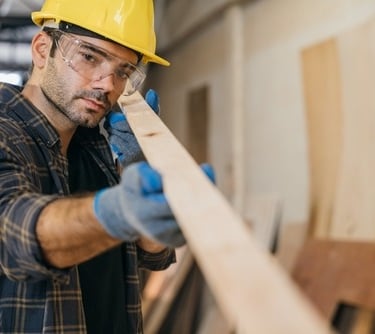 a man in a hard hat and safety glasses is holding a piece of wood