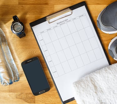 Fitness workout plan on a clipboard with running shoes, water bottle, and gym accessories on a wooden floor.