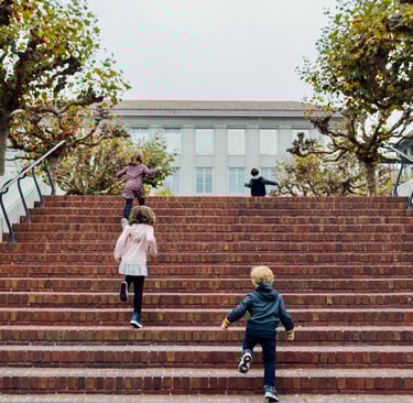 Four small children running up stairs towards a building