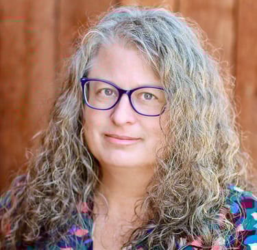 Photo of a woman with long grey, curly hair wearing blue glasses