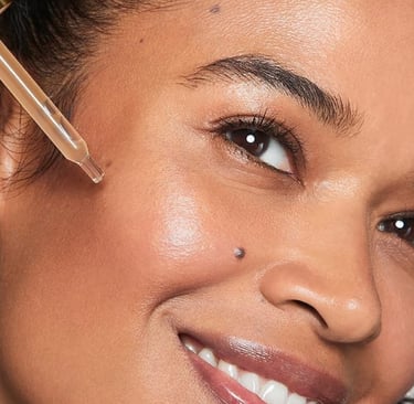 Smiling woman holds a dropper near her cheek, showcasing glowing, moisturized skin.