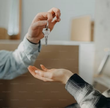 A person handing house keys to a new homeowner with moving boxes in the background.