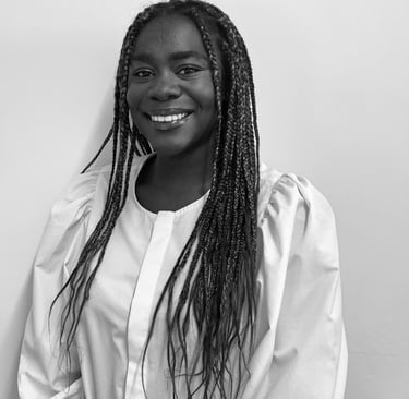 A smiling young Black woman with long braids wearing a white puff-sleeve blouse in a black and white portrait.