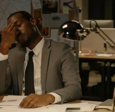 A tired man sitting behind a desk piled with paperwork, looking overwhelmed and exhausted, symbolizing the challenges of work