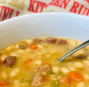 White bowl of navy bean soup with spoon and kitchen towel in the background