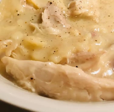 A bowl of old-fashioned Southern chicken and dumplings served in a white bowl with orange spray floral in the background.