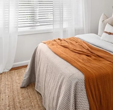 bright bedroom with honey or rust colored throw and pillow with linen rug, fall color