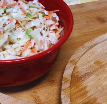 Creamy tangy and sweet coleslaw in a red bowl beside a pulled chicken sandwich on a plate.