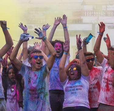 Excited people covered in colorful powder celebrate at a Holi color festival event.