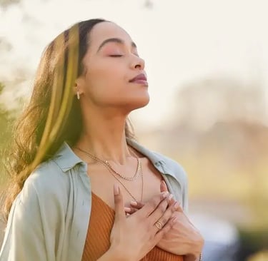 Une femme respire profondément en se tenant debout à l'extérieur, savourant un moment de sérénité et de connexion.