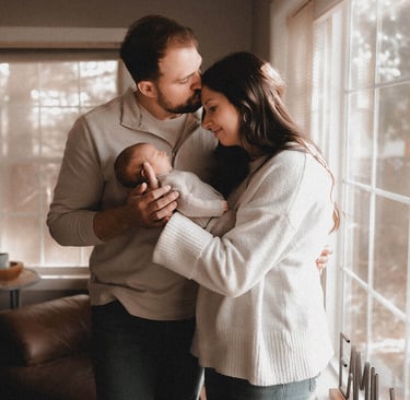 Mom and dad standing by their window with their newborn