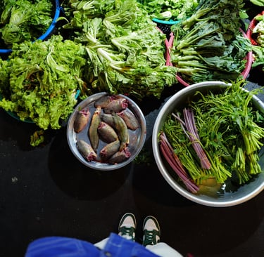 Overhead view of baskets of fresh greens and fish on a market floor, By ACAT Photos.