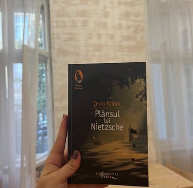 Mână ținând cartea 'Plansul lui Nietzsche' de Irvin Yalom pe un fundal de luminițe de basm.