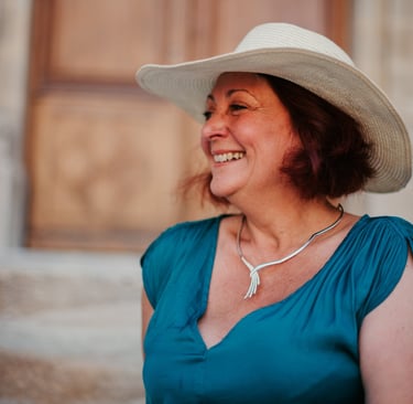 Portrait de Flo Salort assise sur des marches, sourire et chapeau, incarnant liberté et féminité