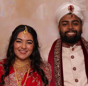 A smiling South Asian couple in traditional wedding attire, featuring a red gold-embroidered sari and a white sherwani