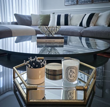 elegant, mirrored, circular coffee table with a tray, books and candles, set against a sofa backdrop