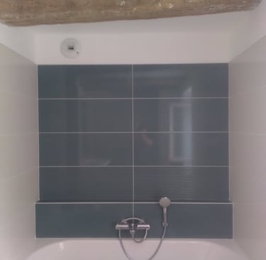 Grande baignoire avec faïences bleu/vert en fond et des retours en beige