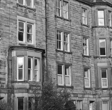 A black and white photo of a traditional stone tenement building featuring bay windows.