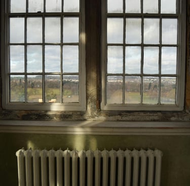 Vintage white radiator sitting below large multi-pane windows 