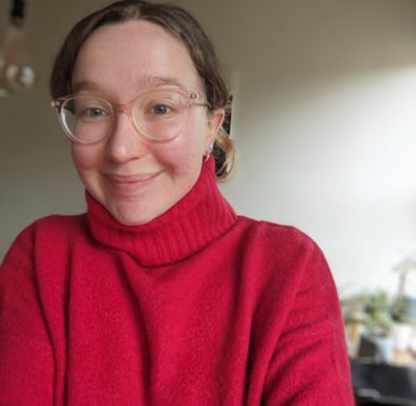 A portrait photograph of female facilitator wearing a red roll neck jumper and glasses