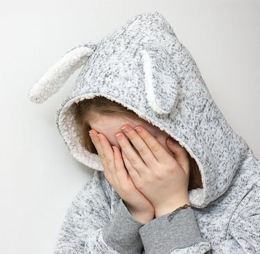 una niña con un suéter gris con orejas de conejo y una sudadera con capucha con la cara tapada