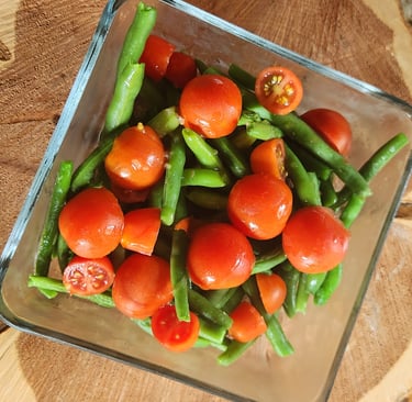 a bowl of green beans and tomatoes on a wooden table