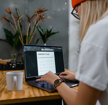 A woman sat on a chair working on her laptop with a cup of coffee by her side
