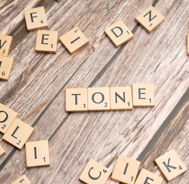 Scrabble pieces laid out on a table spelling the word "tone"