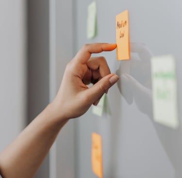 A hand posting a sticky note on a whiteboard during an ideation session