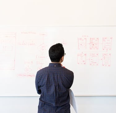 A man looking at a whiteboard displaying a wireframes drawn in red ink.