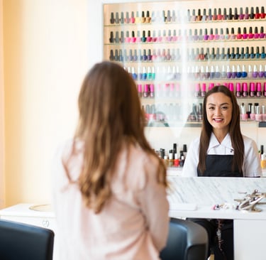 estetista con resto pieno di smalti sorride alla cliente che sta cercando di scegliere lo smalto